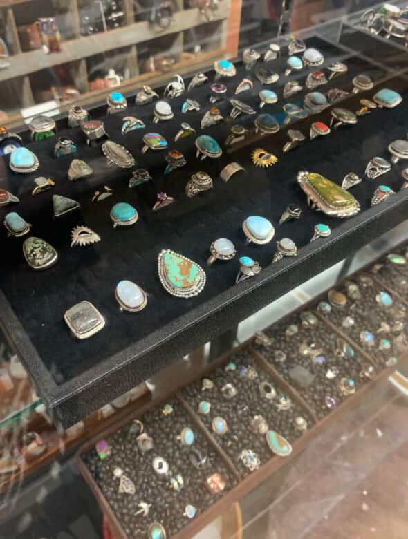 A glass display case is filled with silver rings and other colorful gemstones.