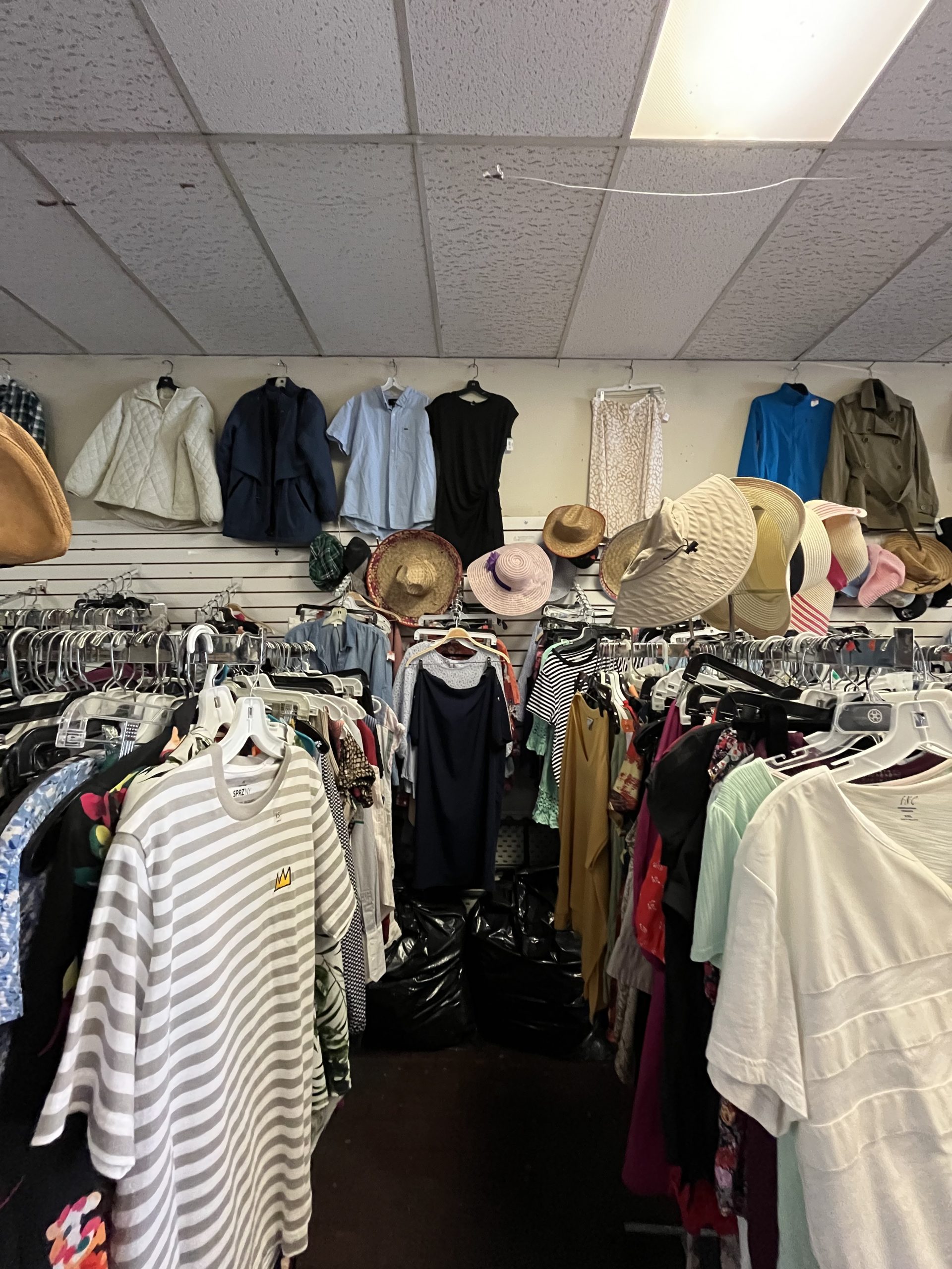 A clothing rack filled with various garments and hats stands beneath more clothes hanging on the wall