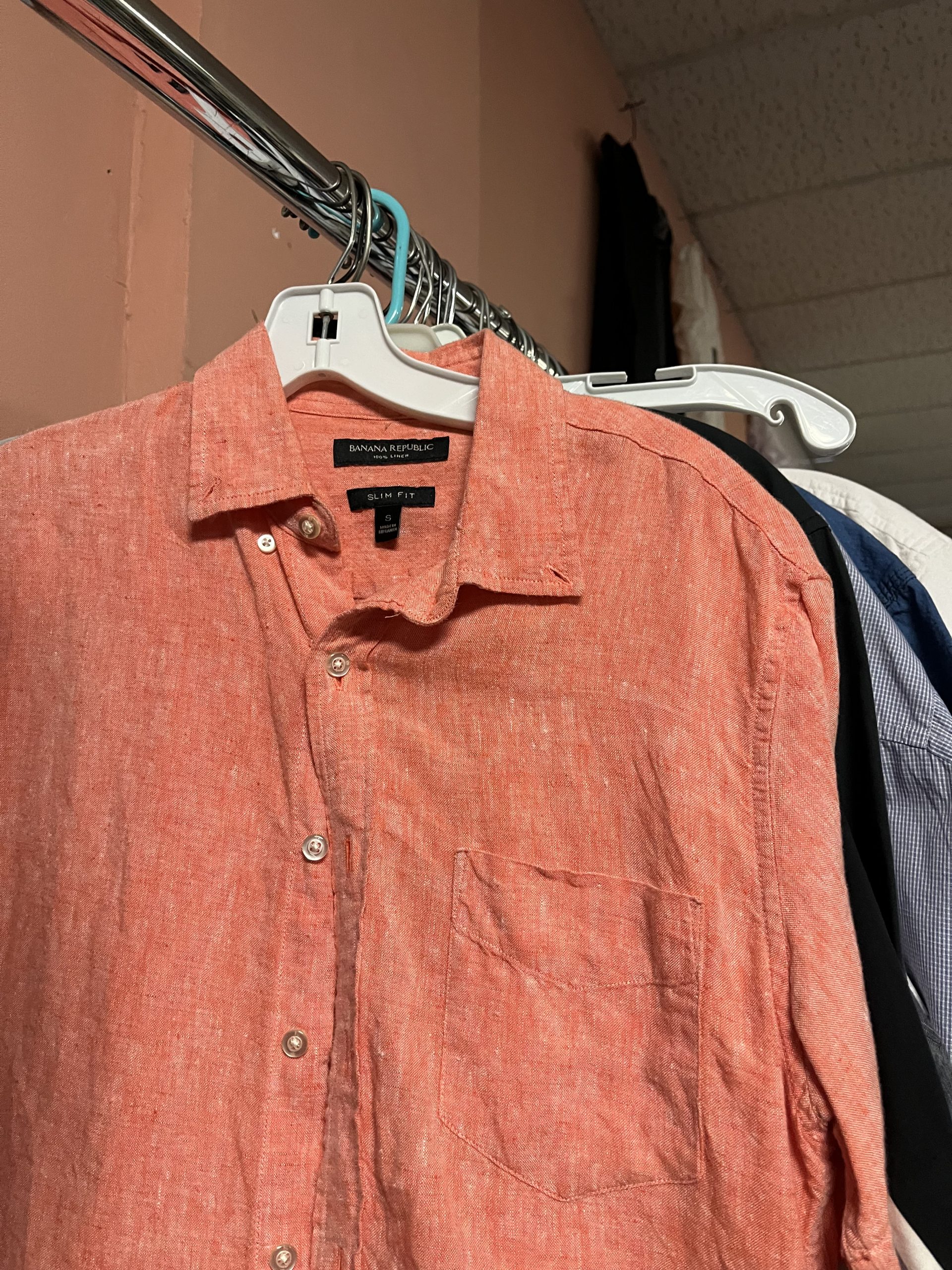 A peach-colored Banana Republic linen shirt hangs on a white hanger on a metal clothing rack